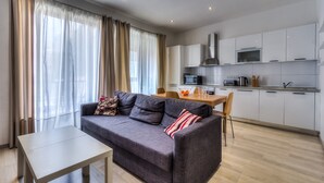 A modern living room with a grey sofa, a small table, and a kitchen area with white cabinets and appliances. - Perfectly Located Sliema Apartment (Sliema)