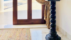 A room with a view of the sea, a wooden door, a patterned curtain, and a bust on a pedestal.