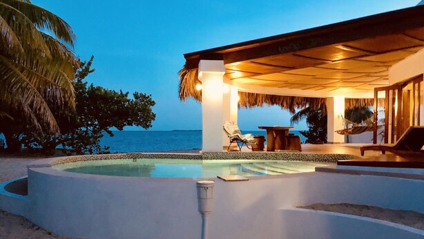 A poolside area with a view of the ocean, a thatched roof structure, and lounge chairs.