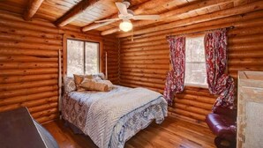 A log cabin bedroom with a bed, a ceiling fan, and a window with curtains. - Cabin in the Pines, Prescott, AZ (Prescott)