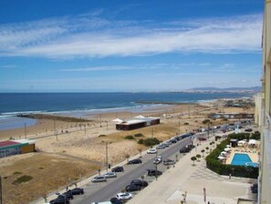 A coastal road with a beach on one side and a resort area with a swimming pool on the other.