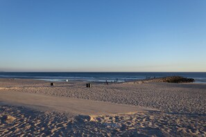 Une plage avec un ciel dégagé, un sol sablonneux et un promontoire rocheux à l’horizon.