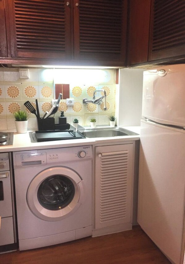 A compact kitchen with a washing machine, a sink, and a refrigerator.