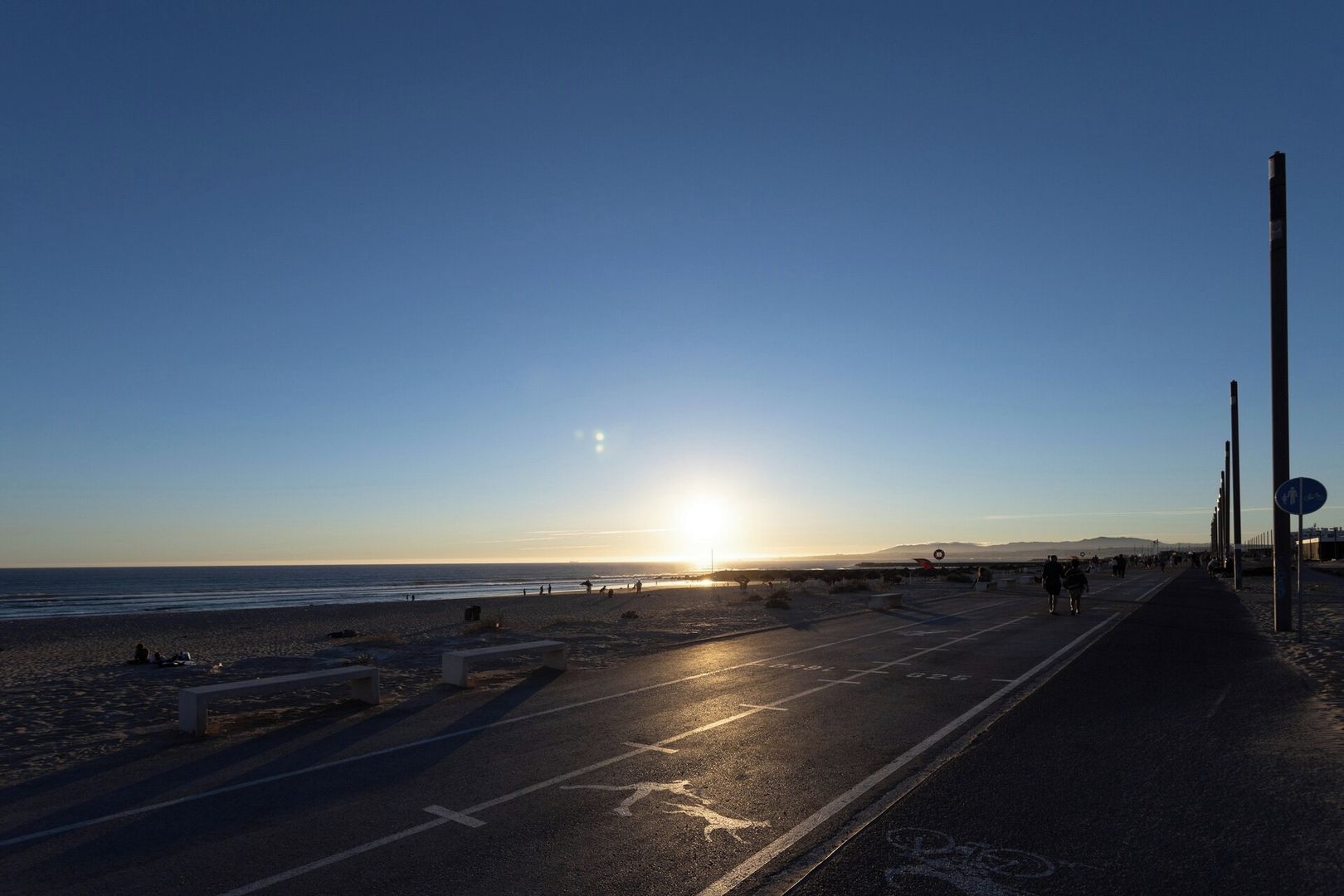 Ein Strand mit einer Straße, Bänken und einem Sonnenuntergang.