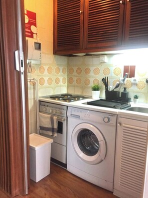 A compact kitchen with a washing machine, oven, and a small countertop with a sink. - Wonderful apartment right on the beach (Costa da Caparica)
