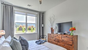 Ein Schlafzimmer mit einem Bett, einer Holzkommode, einem Fernseher und einem Fenster mit Vorhängen.