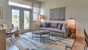 Ein Wohnzimmer mit Sofa, Couchtisch und Sesseln. An der Wand hängt ein Gemälde und auf einem Beistelltisch steht eine Lampe.