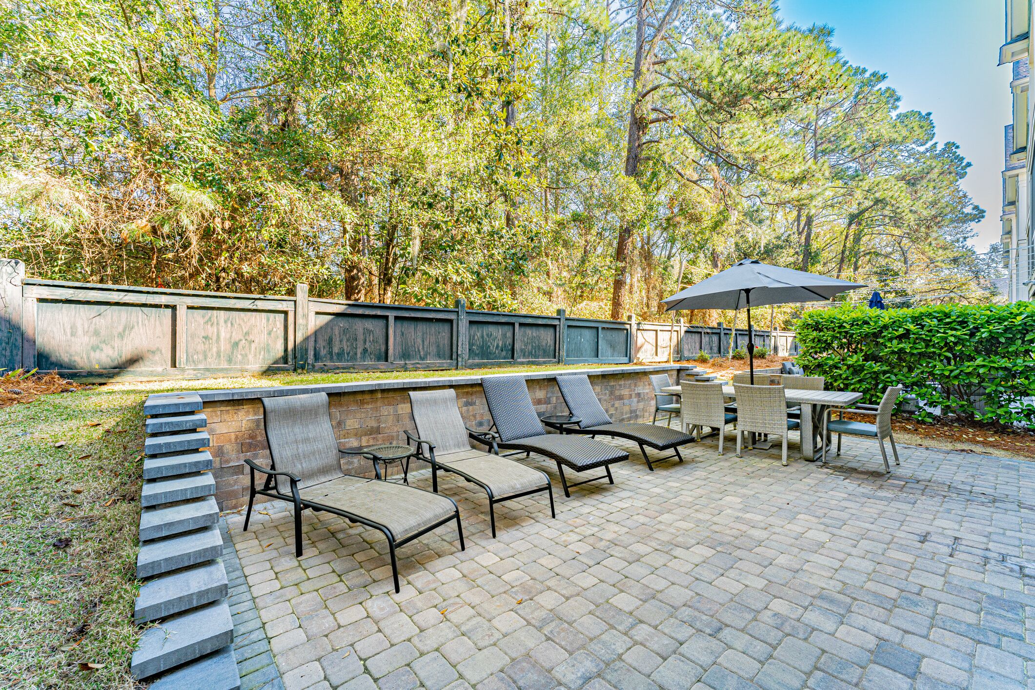 An outdoor patio with stone steps leading to a seating area with chairs and tables, surrounded by trees and a building in the background.