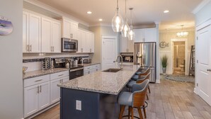 A modern kitchen with white cabinets, granite countertops, and a central island with bar stools. - 115 Luxury Pool Home | Elevator | Kid's Playroom (Hilton Head Island)