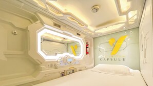 Habitación de hotel cápsula con cama, espejo, panel de control y una pared con un logotipo amarillo.