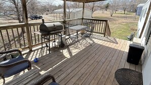 A covered deck with wicker furniture, a grill, and a view of the surrounding area.