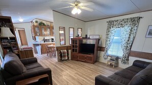 A living room with a wooden floor, two sofas, a TV stand, and a ceiling fan.