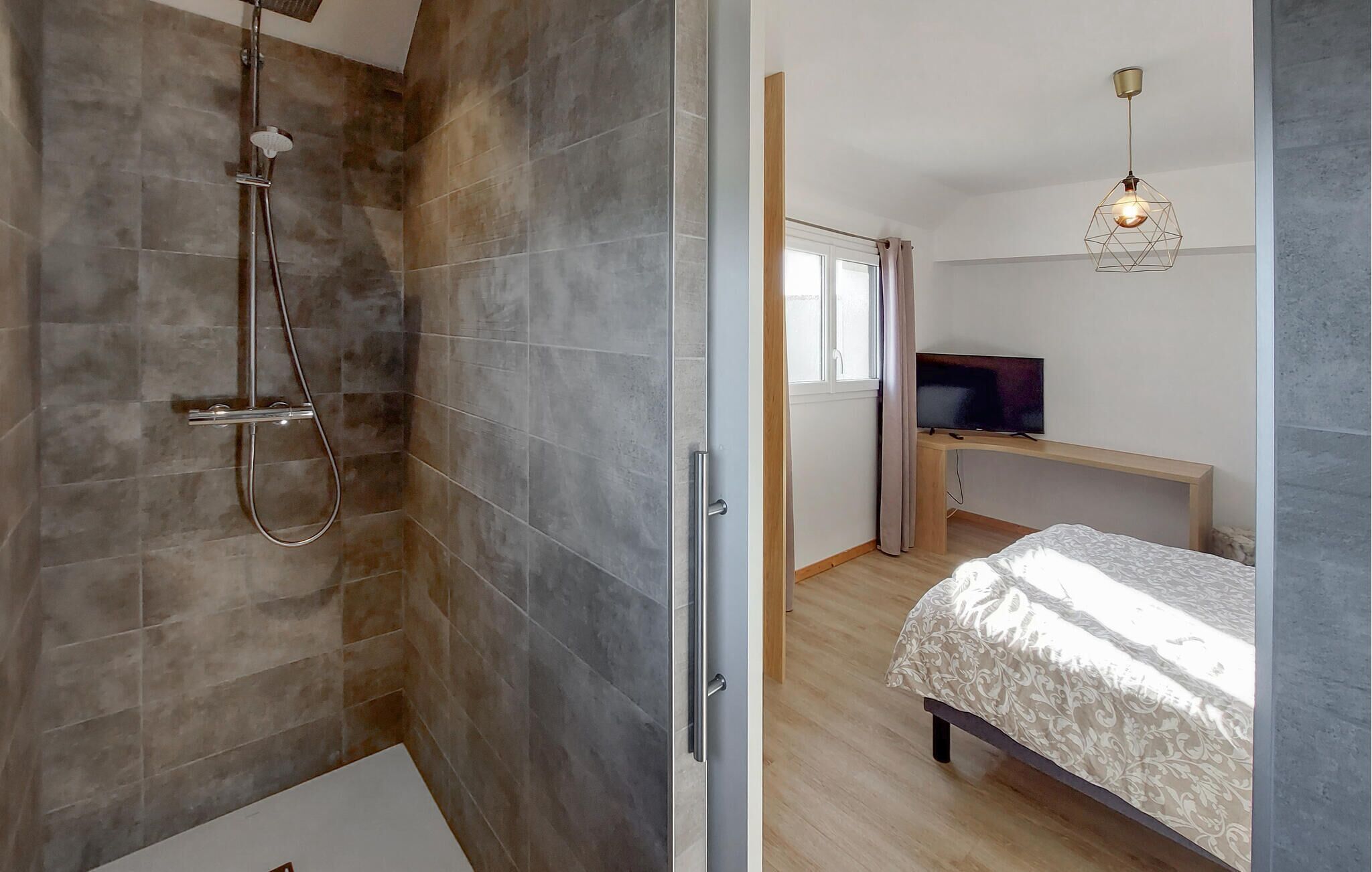 A modern bathroom with a shower and a separate toilet. There is a bed with a patterned bedspread and a TV on a wooden stand.