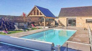 Una piscina con bordo in legno, sedie a sdraio e un edificio in pietra con tetto blu.