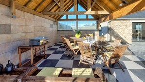 Un'area pranzo all'aperto coperta, con mobili in legno, un barbecue e vista sul paesaggio.