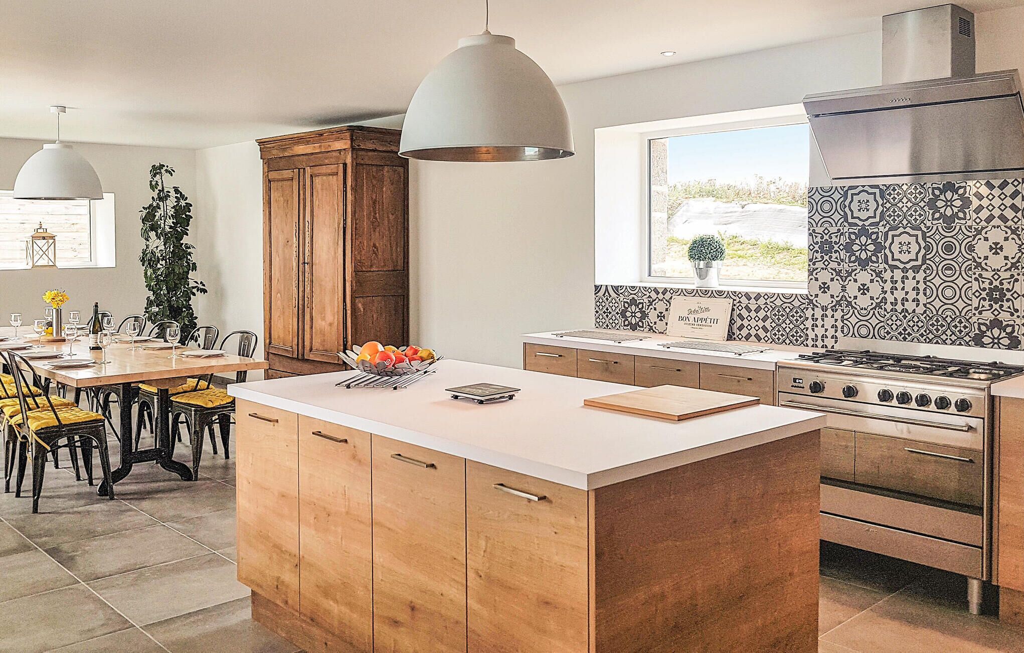 A modern kitchen with a central island, wooden cabinets, a gas stove, and a patterned backsplash.