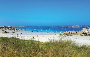 A beach with clear blue water, rocky shoreline, and sparse vegetation.