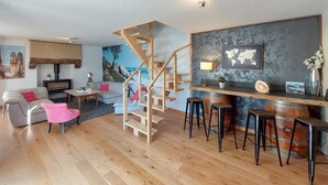 Un soggiorno moderno con una scala in legno, un angolo bar con sgabelli, un divano grigio e una grande mappa del mondo appesa al muro.