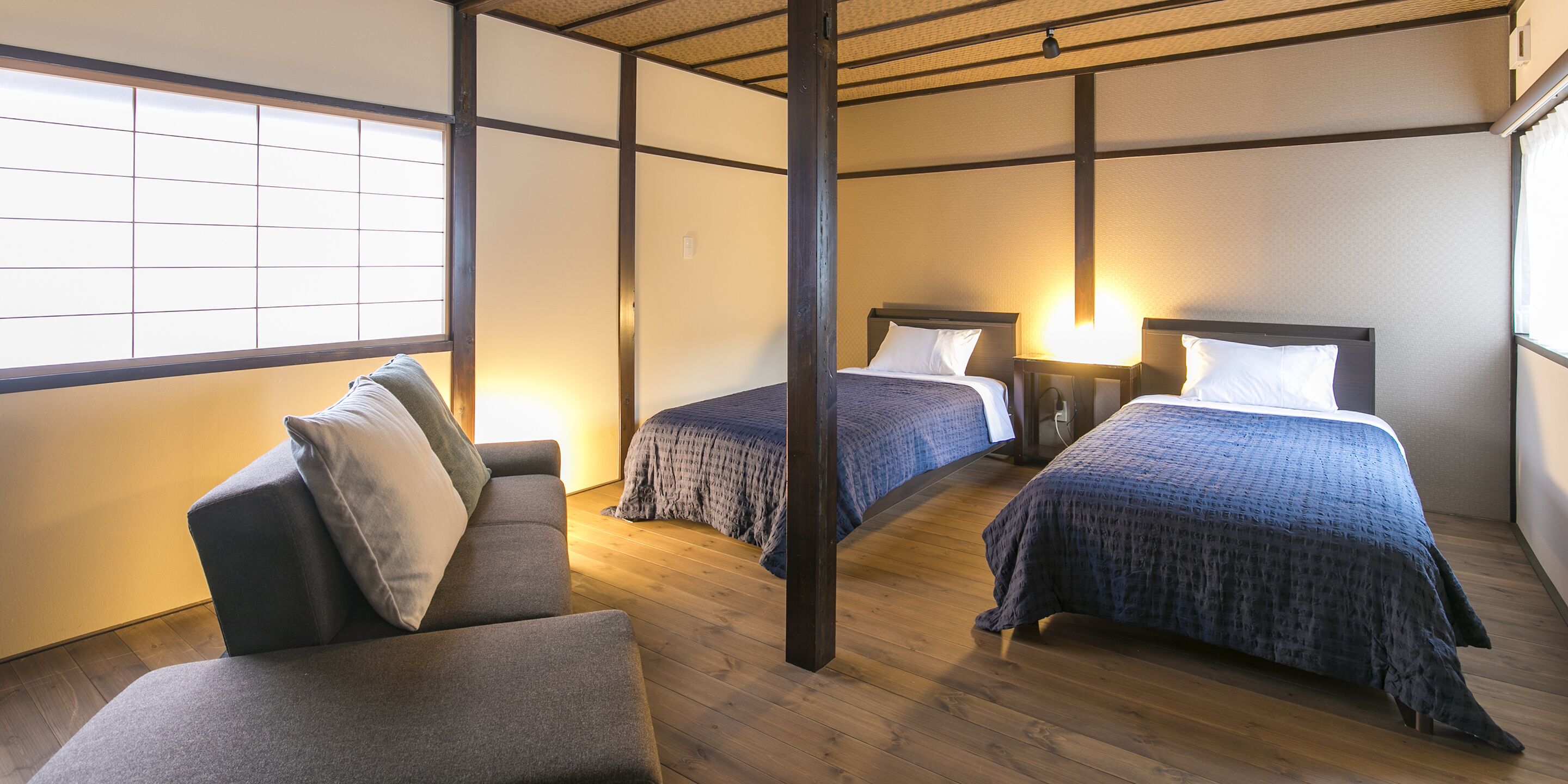 A traditional Japanese-style room with two beds, a sofa, and a wooden floor.