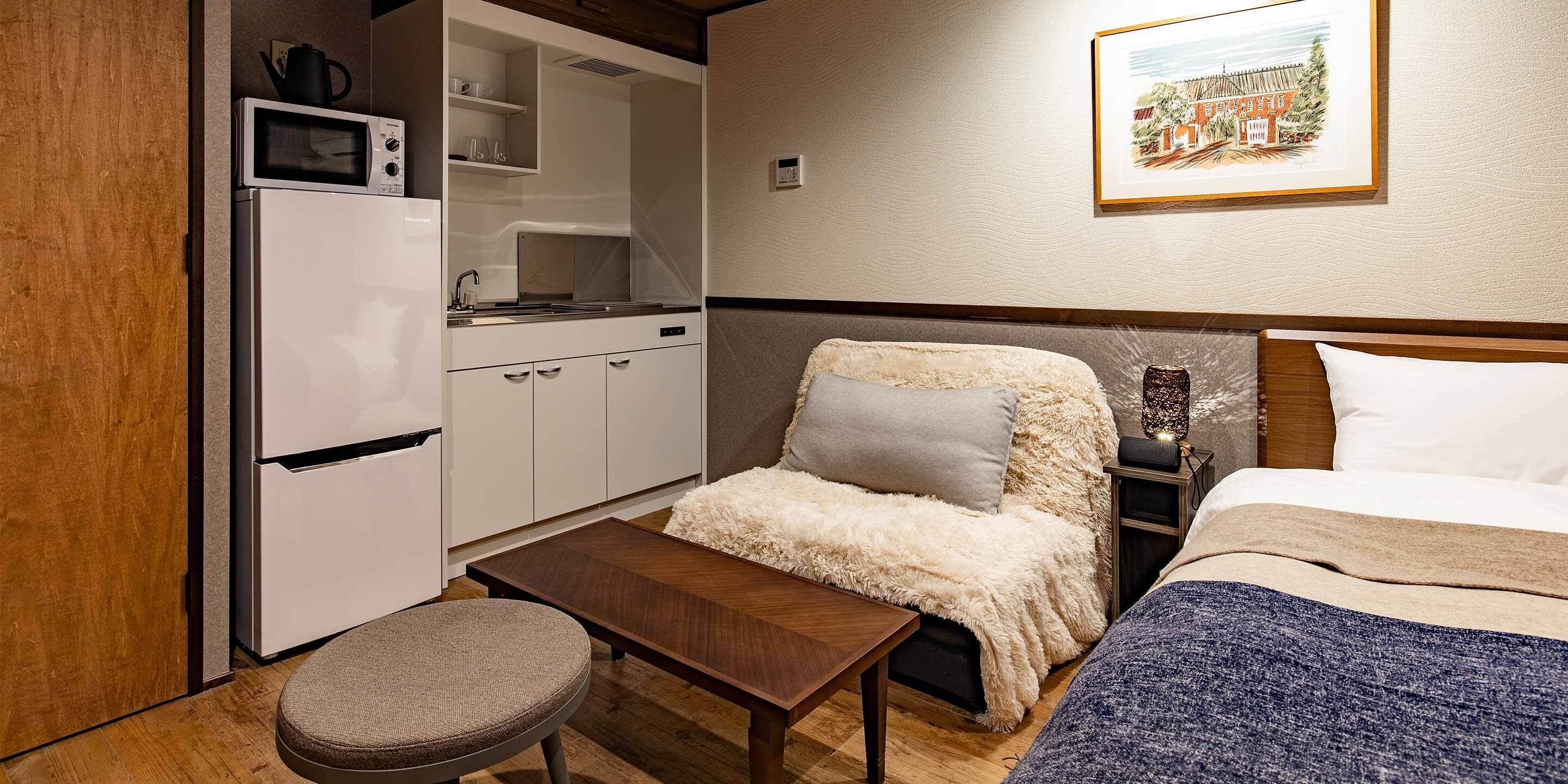 Habitación de hotel compacta con kitchenette, una cama con manta mullida y una pequeña mesa.
