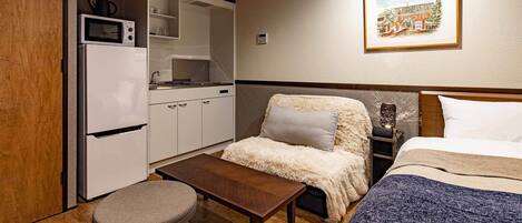 Habitación de hotel compacta con kitchenette, una cama con manta mullida y una pequeña mesa.