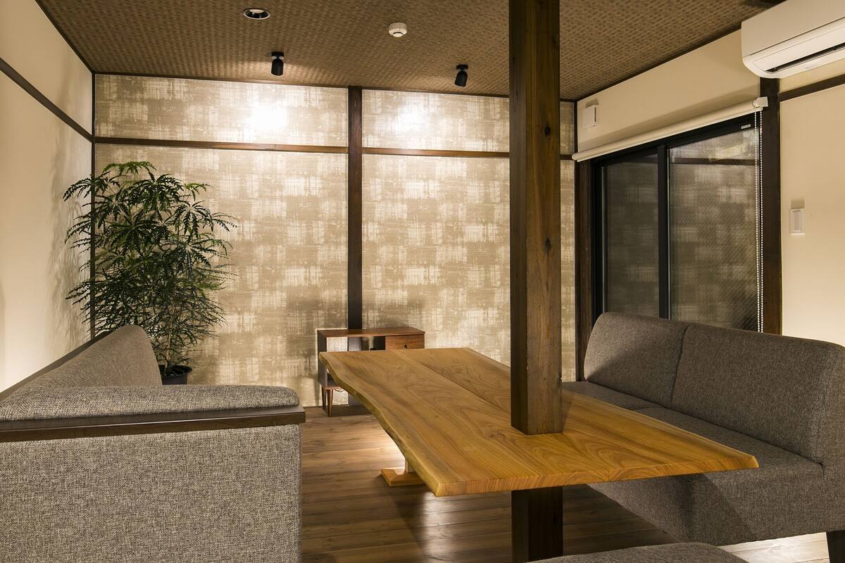 A modern interior with a wooden dining table, grey upholstered seating, and a large potted plant.