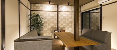 A modern interior with a wooden dining table, grey upholstered seating, and a large potted plant.