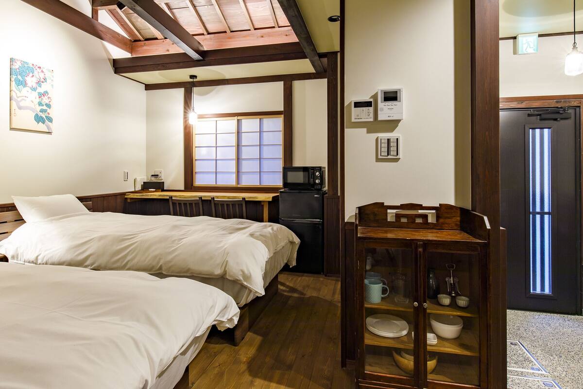 A hotel room with two beds, a wooden cabinet, a window, and a door with a light fixture.