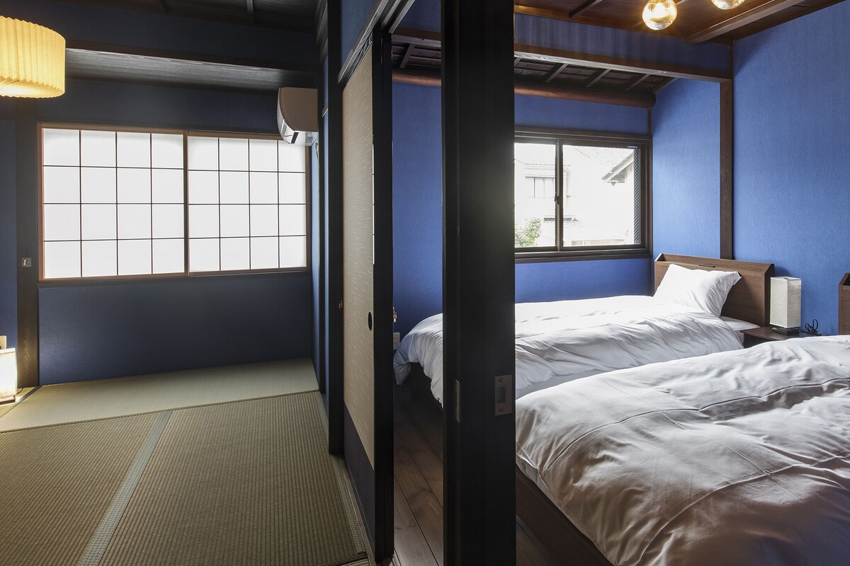 A room with two beds, a tatami mat floor, and a window with a view of the outside.