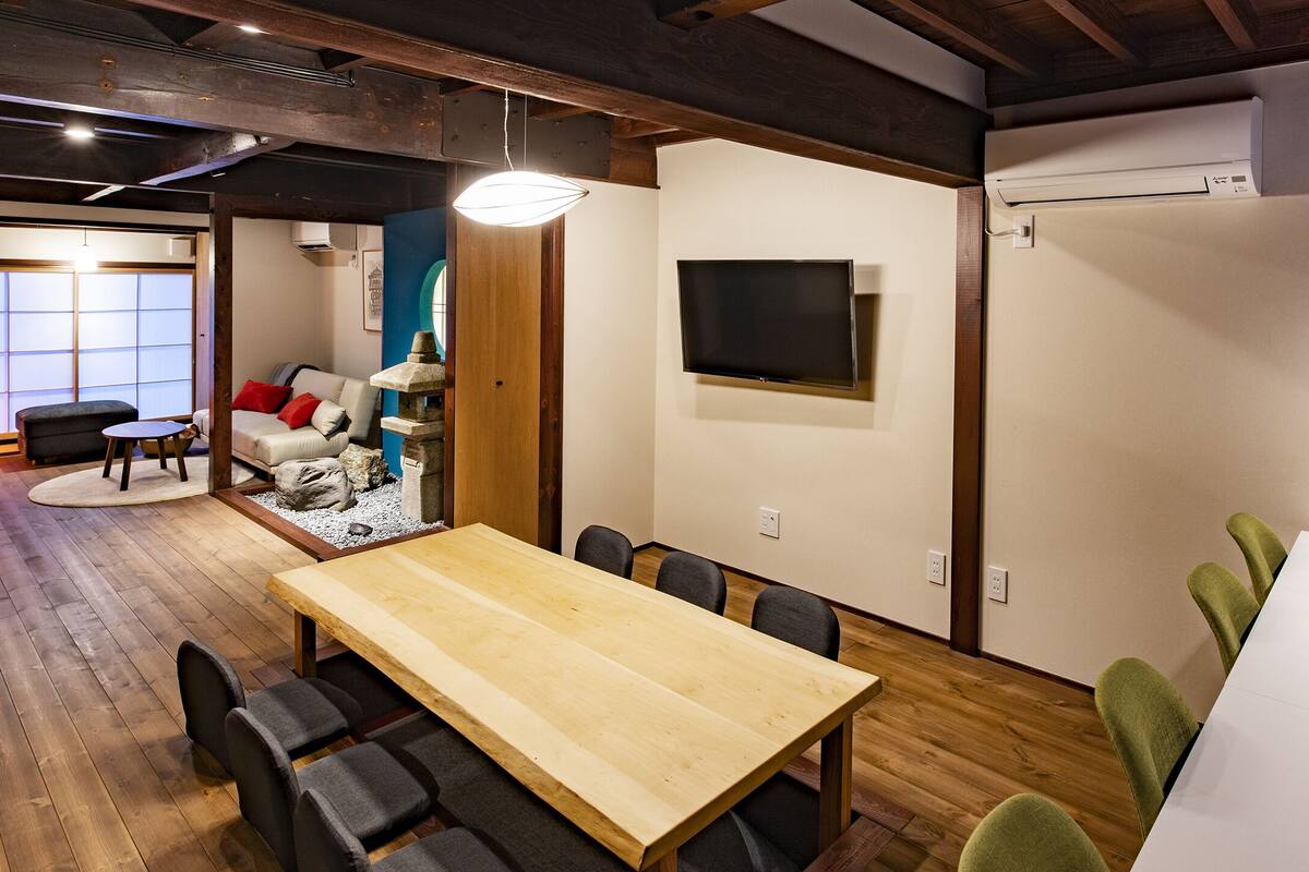A modern meeting room with a wooden table, chairs, and a TV on the wall.
