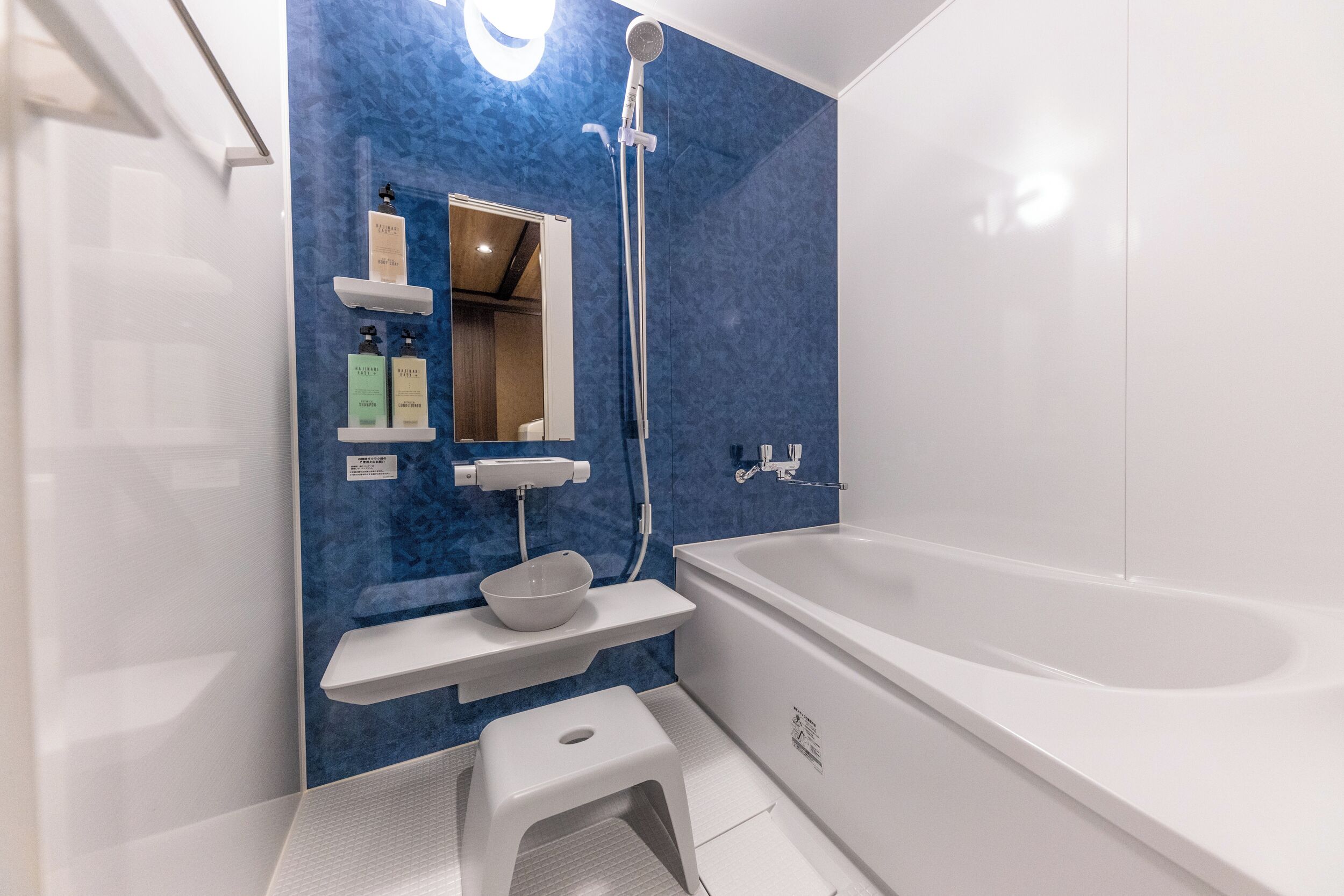 Un bagno moderno con una vasca da bagno ampia, un lavandino bianco con uno specchio sopra e una parete di accentuazione blu.