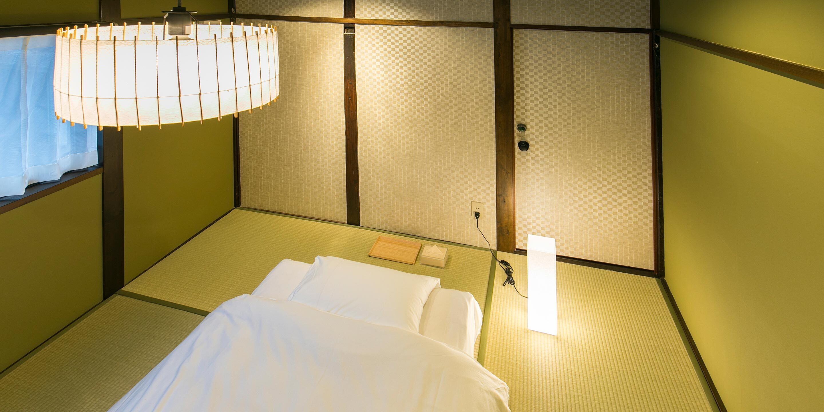 A traditional Japanese-style room with tatami flooring, a bed with white bedding, a hanging lamp, and a shoji screen.