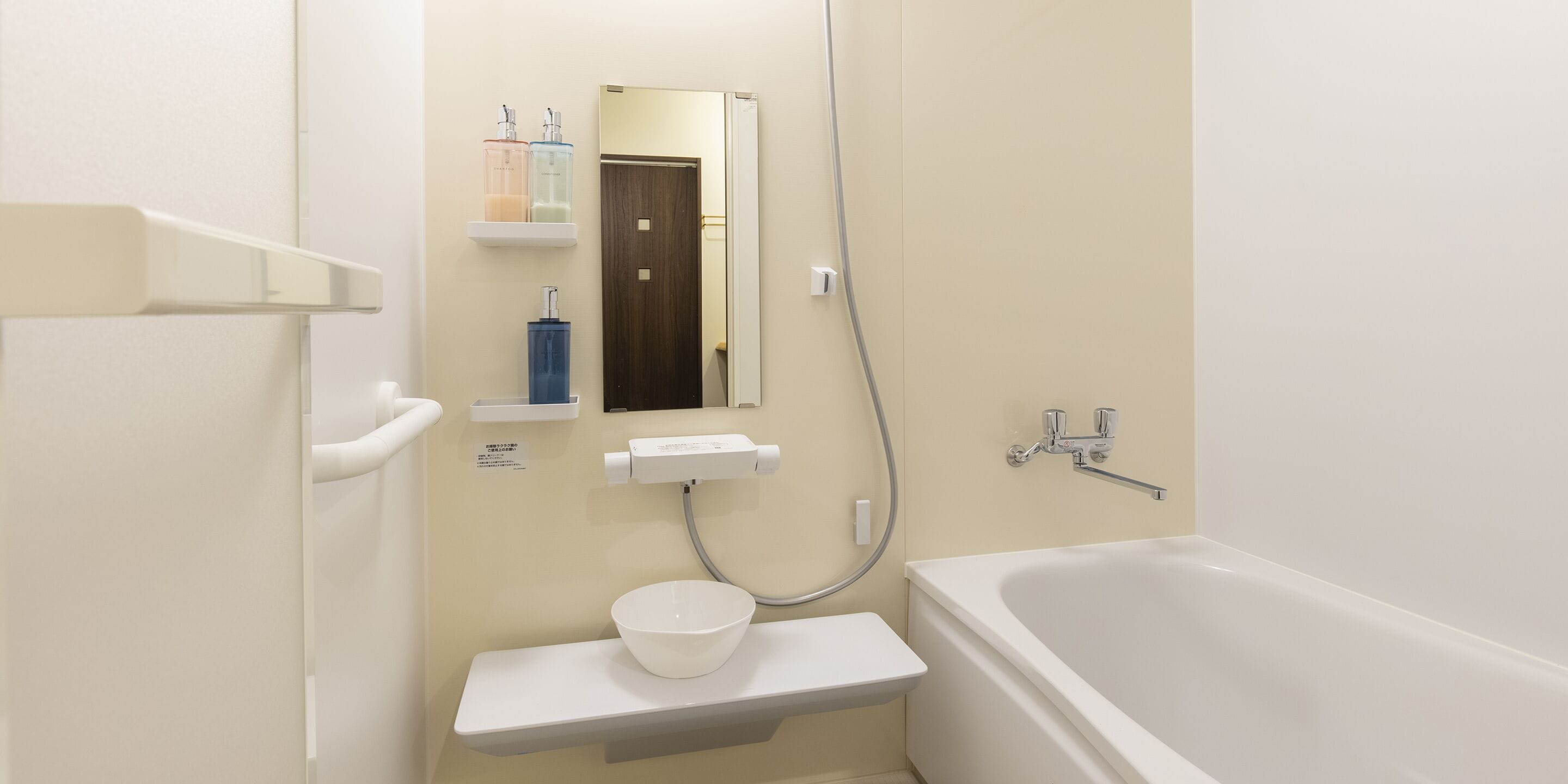 A bathroom with a bathtub, a sink with a soap dispenser, a mirror, and a showerhead.