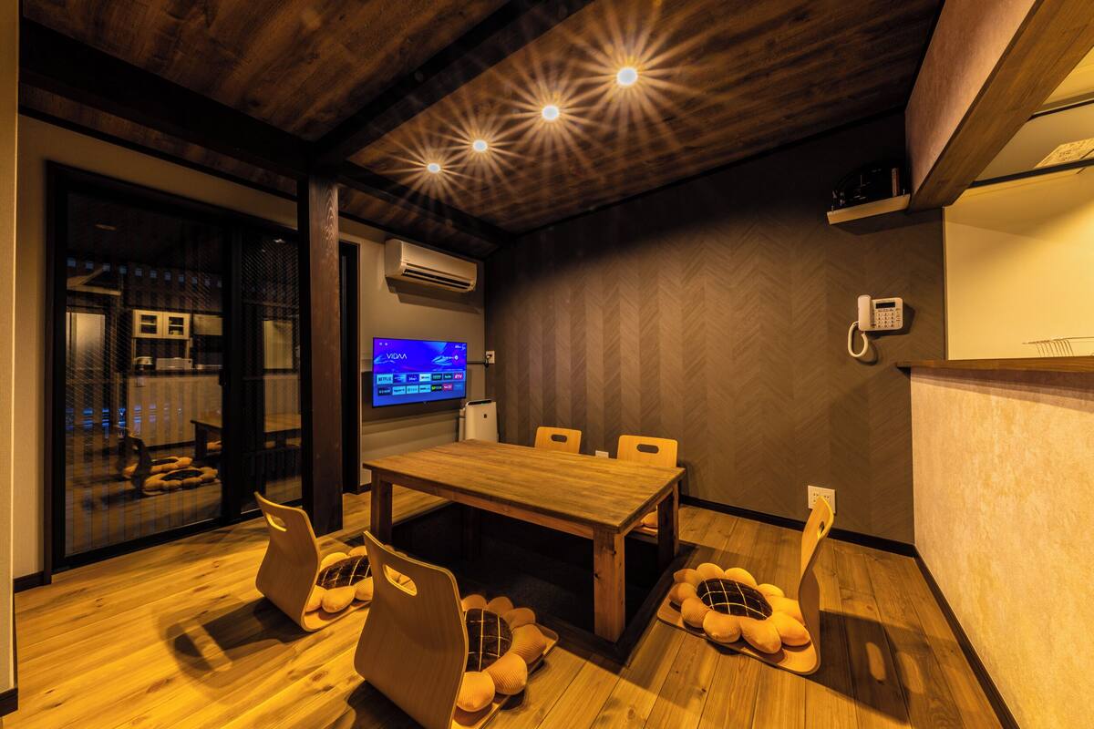 A modern room with a wooden dining table, cushioned chairs, a flat-screen TV, an air conditioning unit, and a telephone.