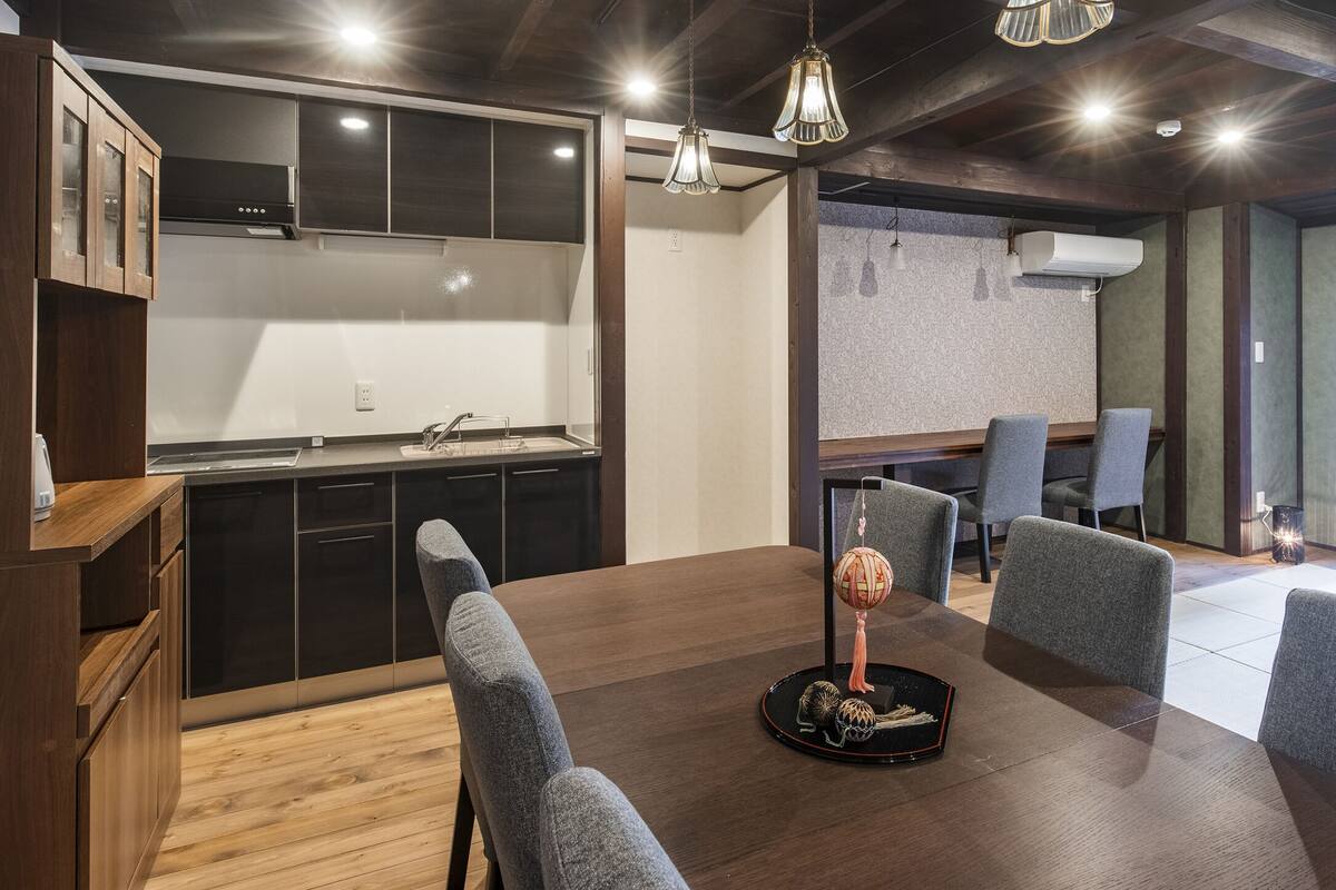 A modern kitchen with dark cabinets, a wooden dining table, and a seating area with grey chairs.