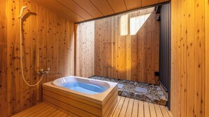 Un spa con sala de madera, bañera de hidromasaje, suelo de madera y un sendero de piedra.