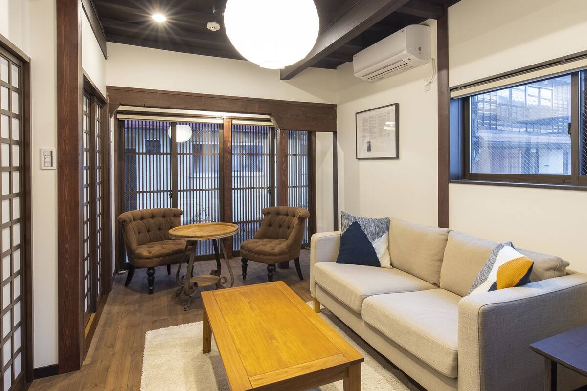 A traditional Japanese-style room with tatami flooring, a low table, a sofa with cushions, and a sliding door with a grid pattern.