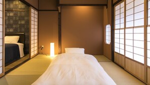 Una habitación tradicional japonesa con suelo de tatami, futón bajo y puertas correderas shoji.