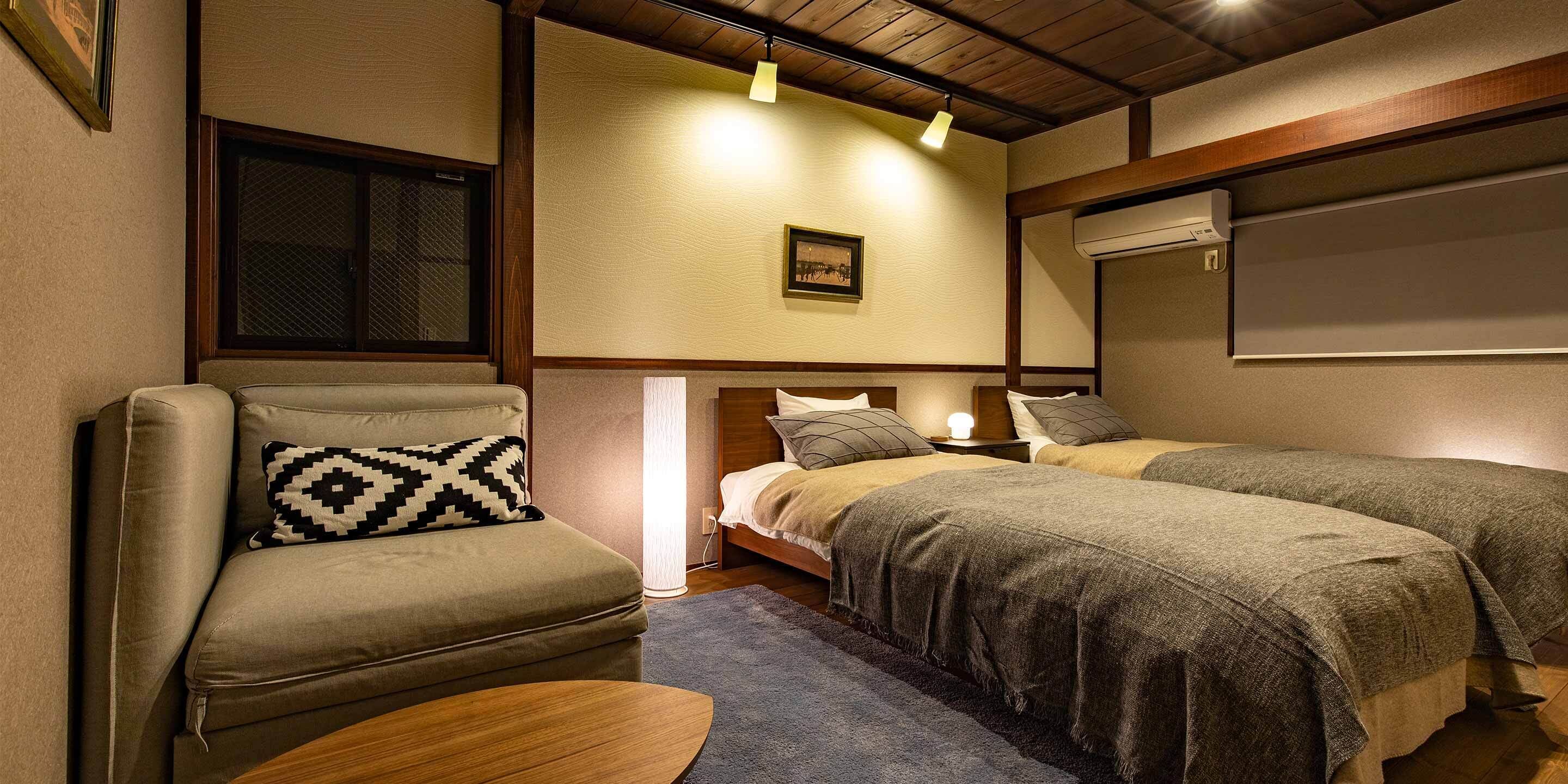 A cozy room with a sofa, two beds, a nightstand, and a wall-mounted air conditioner.