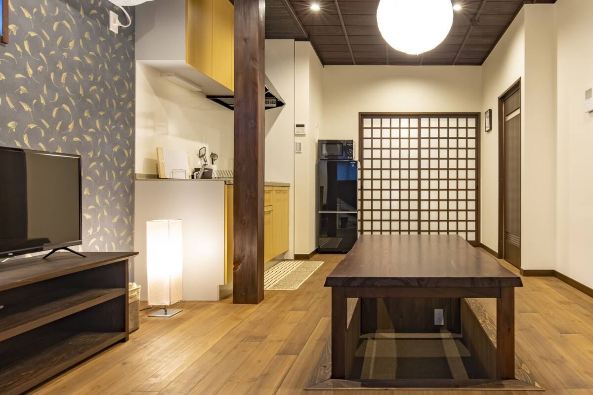 A modern living room with a wooden floor, a TV stand, a table, and a cabinet with shelves.
