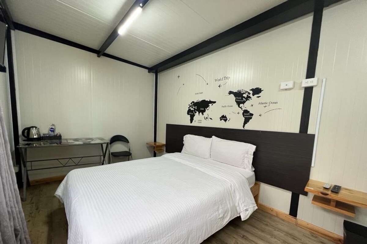 A bedroom with a bed, a desk, a chair, and a world map on the wall.