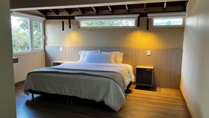 Un dormitorio moderno con una cama grande, cabecera de madera, mesitas de noche y vistas a zonas verdes por la ventana.