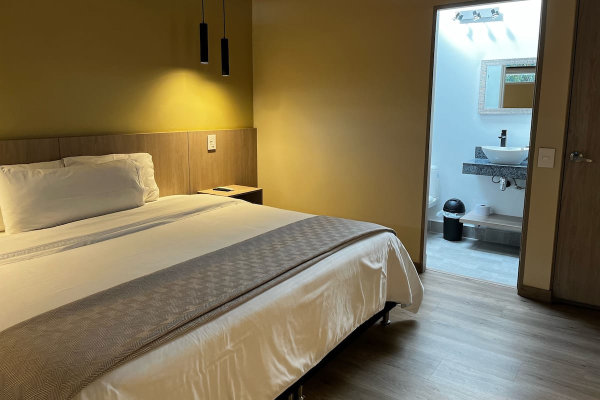 A hotel room with a bed, bedside table, and a view of the bathroom.