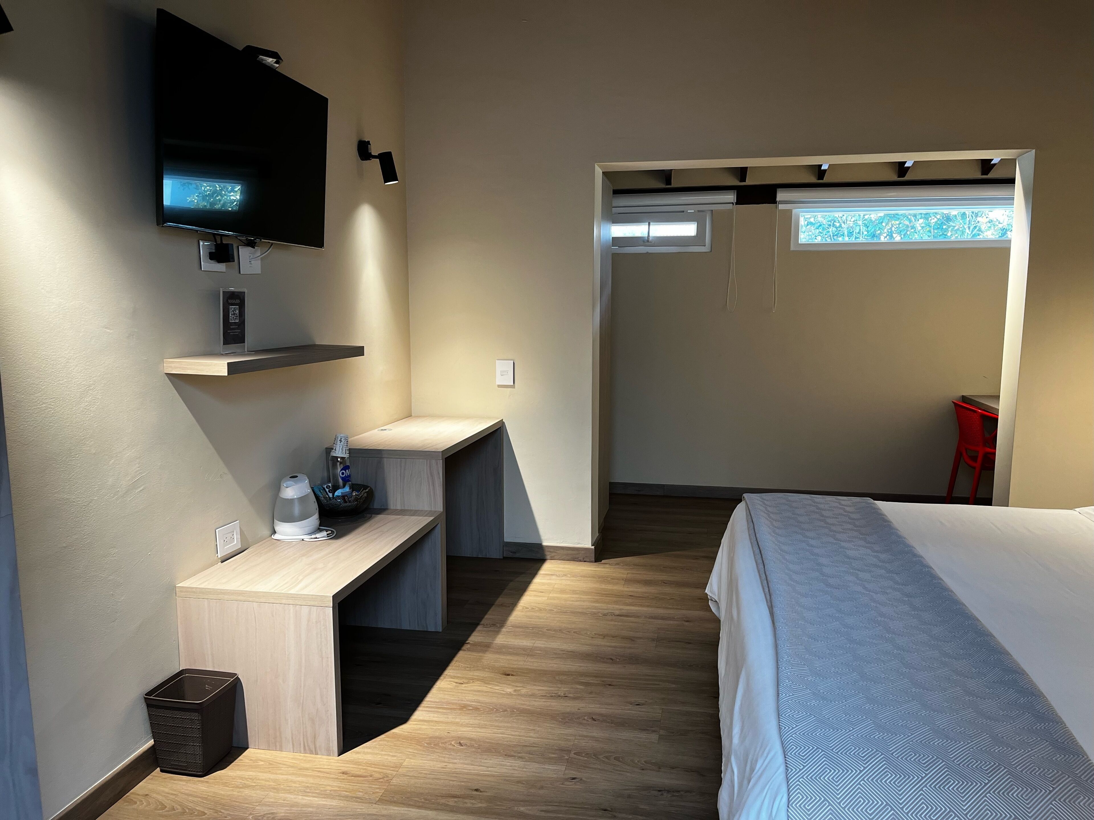 Une chambre d’hôtel moderne équipée d’un lit, d’un bureau, d’un téléviseur fixé au mur et d’une petite fenêtre.