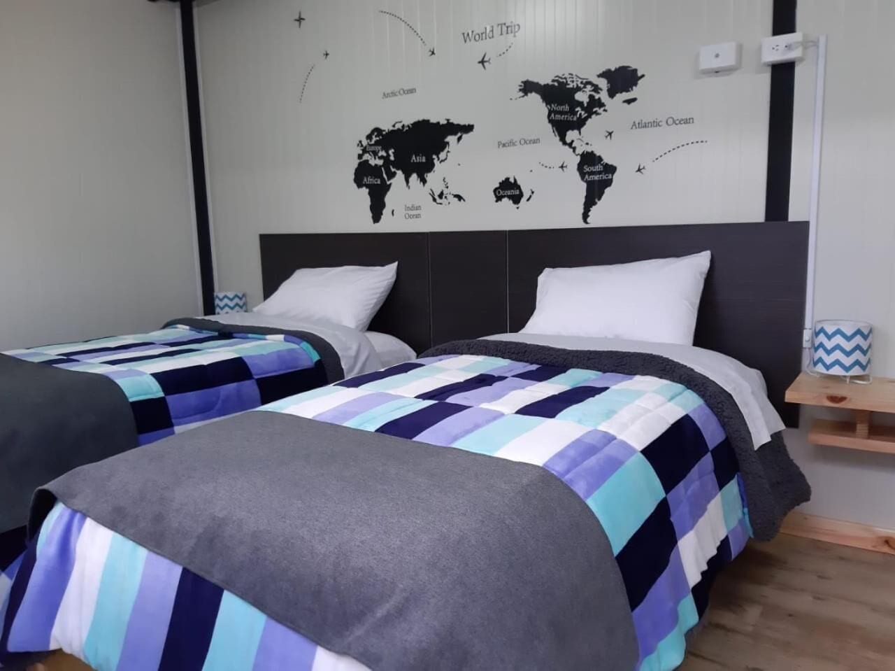 Una habitación de hotel con dos camas, un mapa mundial en la pared y una mesita de noche de madera.