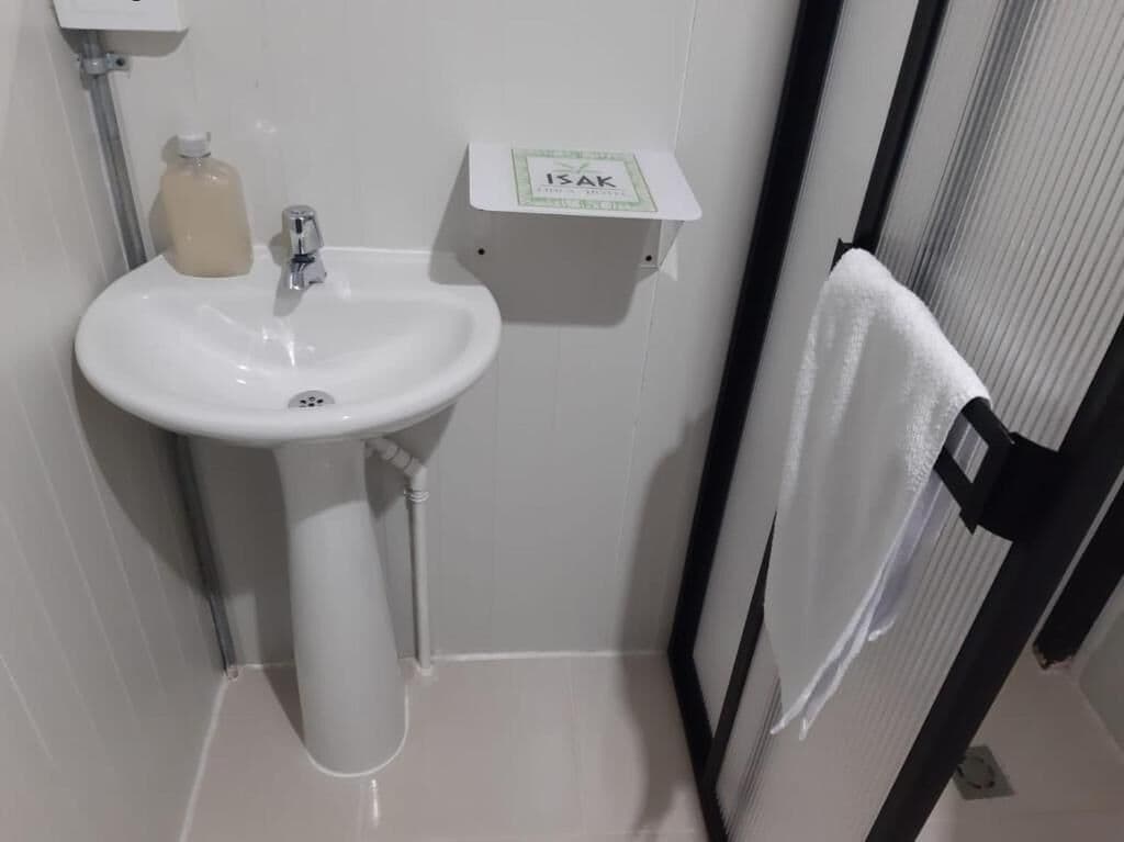 Un baño con un lavamanos blanco, un dispensador de jabón y un porta papel higiénico con el rótulo 'ISAK'.