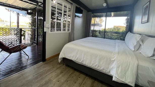 Un dormitorio con una cama grande, una silla y vistas a través de un ventanal.