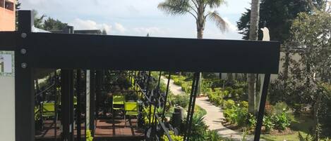 Un jardin doté d’une terrasse en bois, de palmiers et d’un portail en métal.