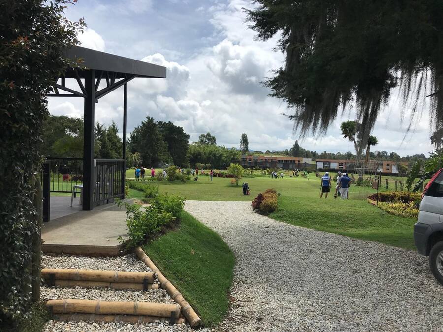 Um campo de golfe com um pavilhão, caminhos de cascalho e um edifício ao fundo.