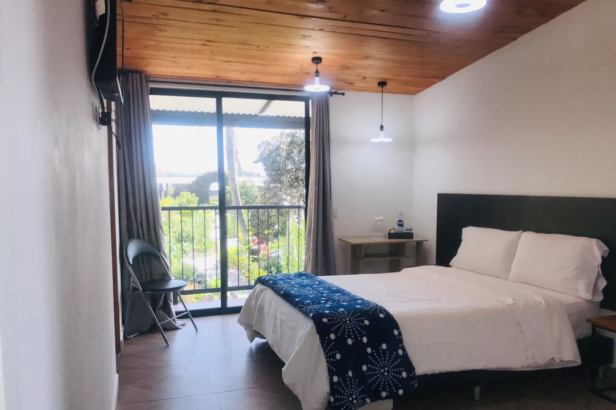 A bedroom with a bed, a chair, a nightstand, and a view of a garden through a sliding door.